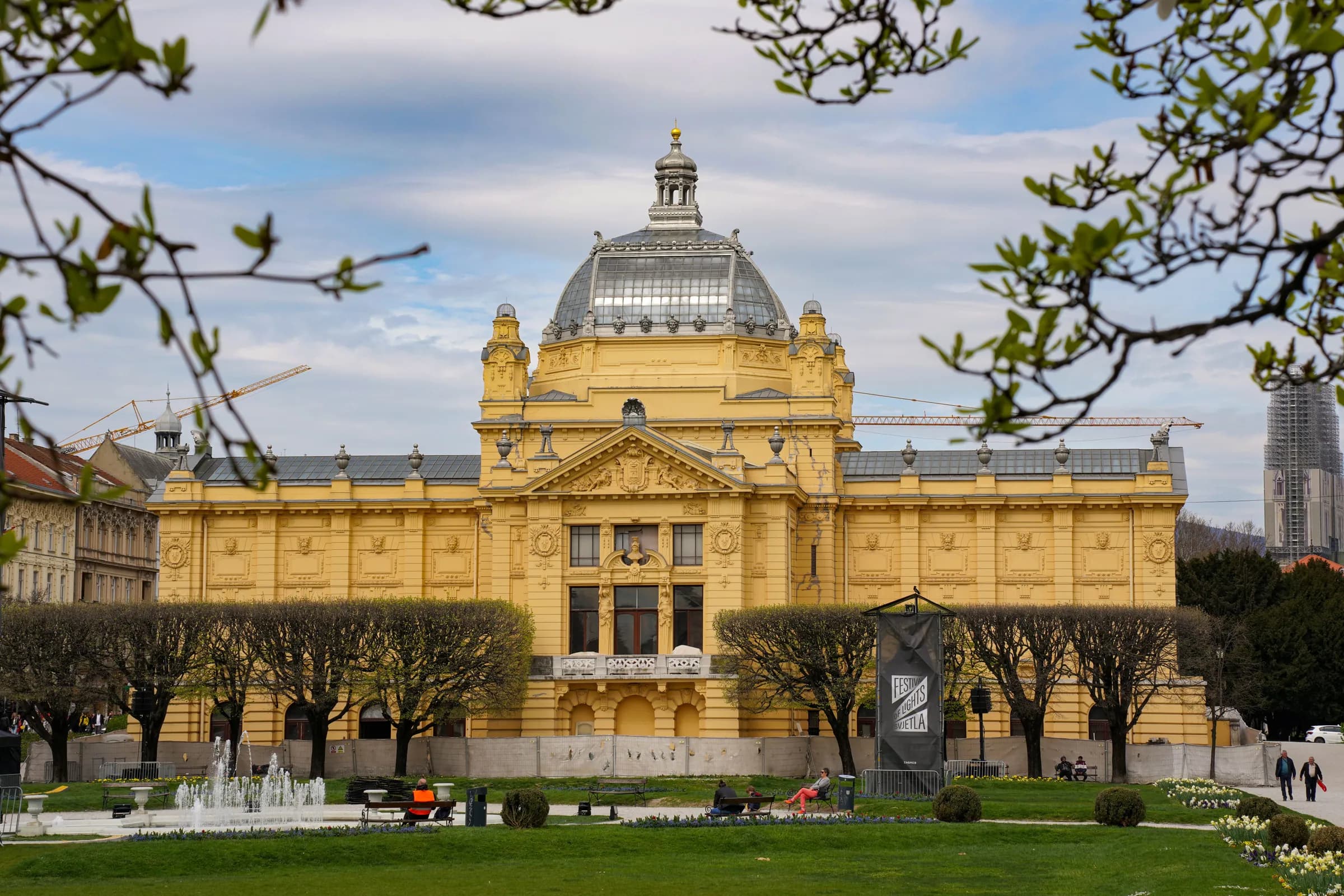 Il Padiglione dell'Arte giallo nel centro di Zagabria, visto tra i rami primaverili